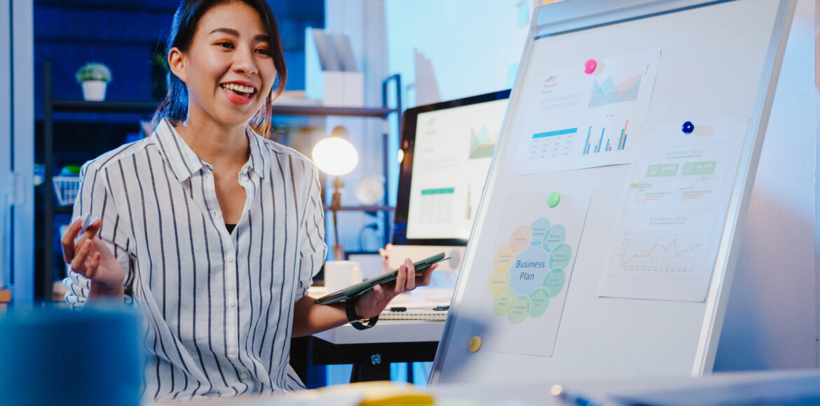 Asia businesswoman social distancing in new normal for virus pre Asia businesswoman social distancing in new normal for virus prevention looking at camera presentation to colleague about plan in video call while work in office night. Lifestyle after coronavirus.