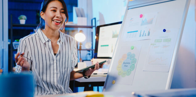 Asia businesswoman social distancing in new normal for virus pre Asia businesswoman social distancing in new normal for virus prevention looking at camera presentation to colleague about plan in video call while work in office night. Lifestyle after coronavirus.